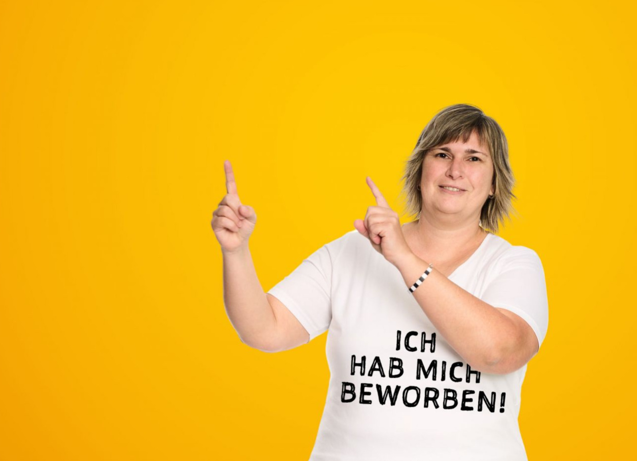Eine Frau zeigt über ihre Schulter nach oben. Auf ihrem Shirt steht